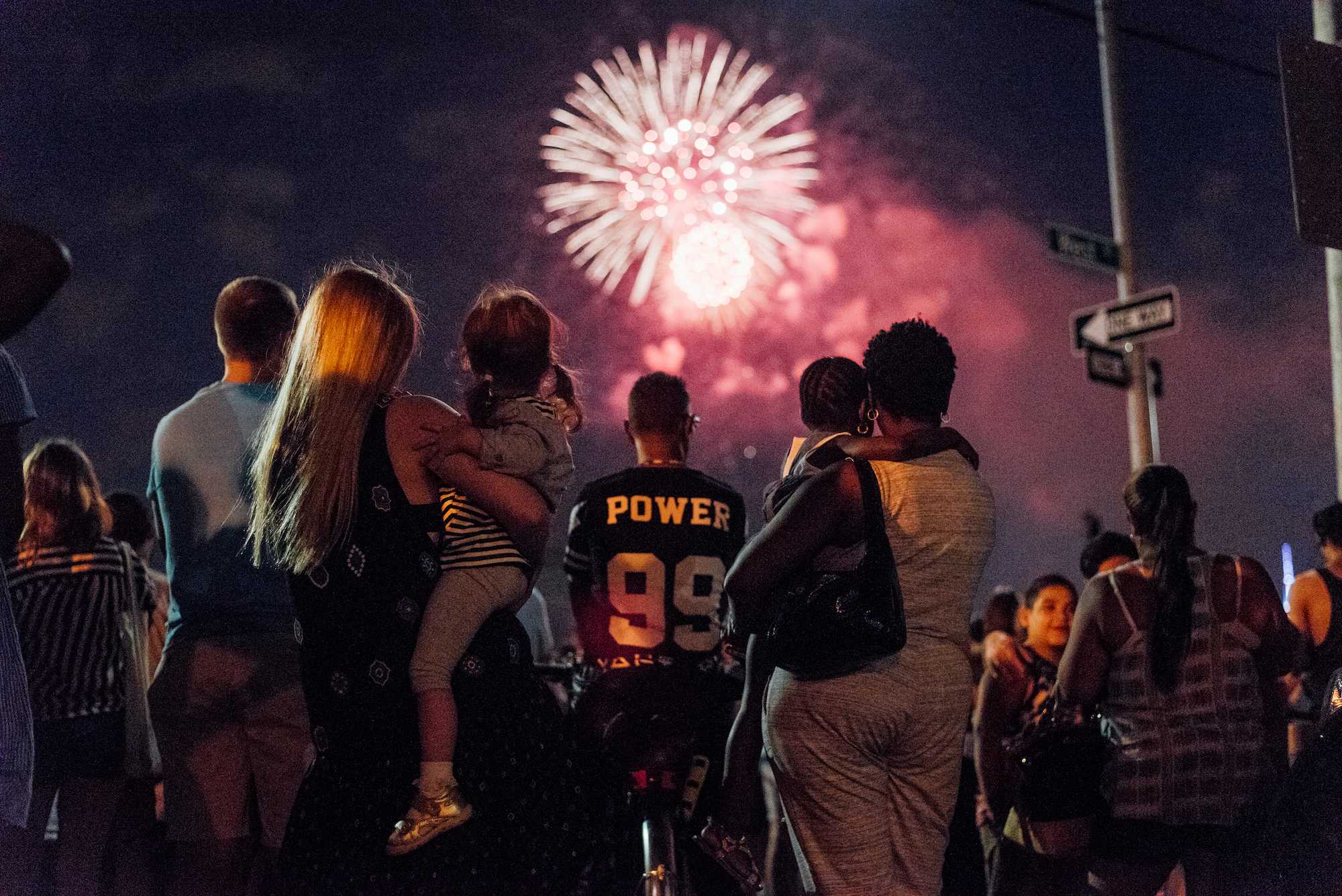 Two mothers hold their daughters while watching July 4th fireworks over the East River.
