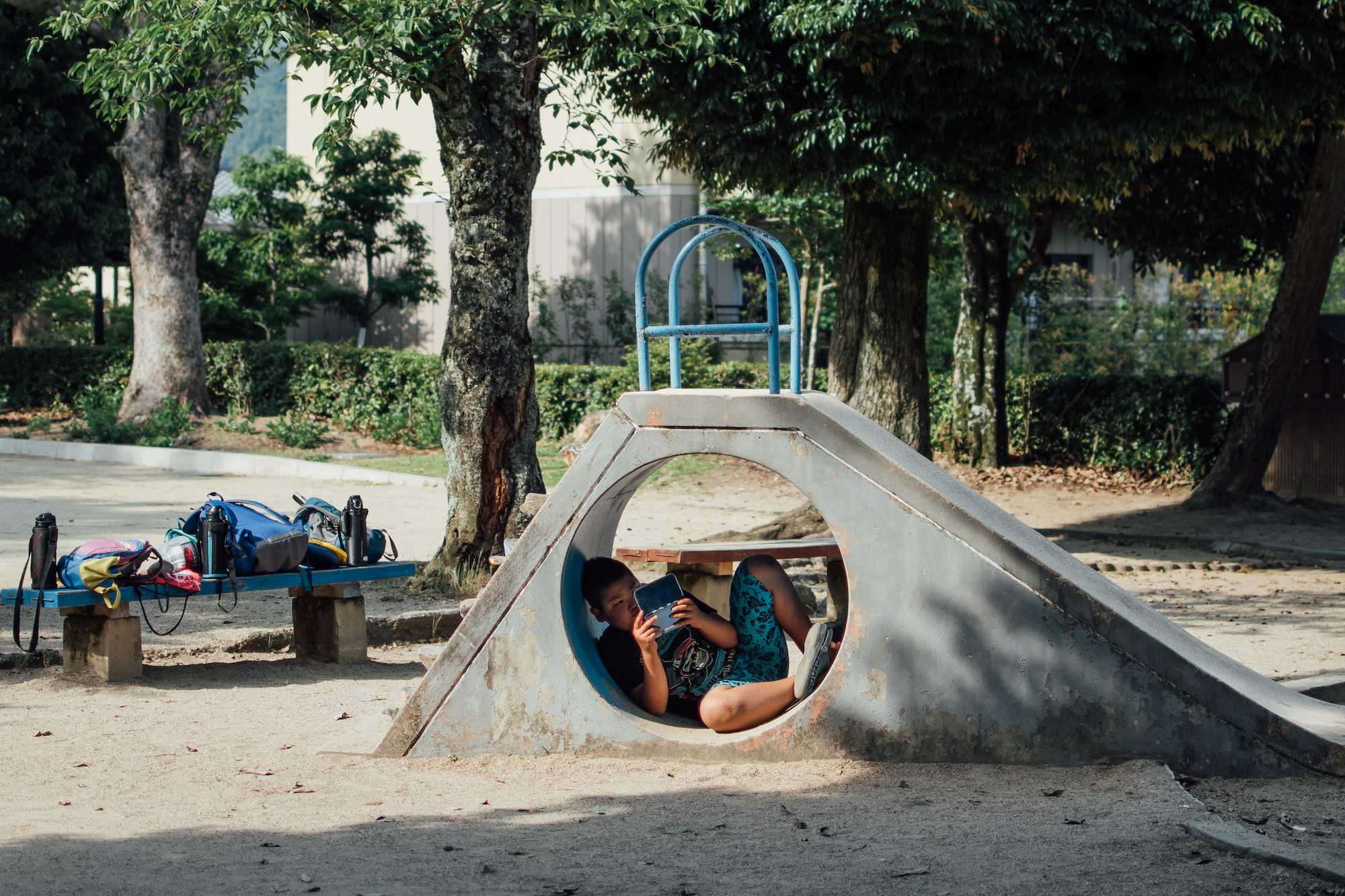 A boy curls up underneath a slide to play his Nintendo DS.